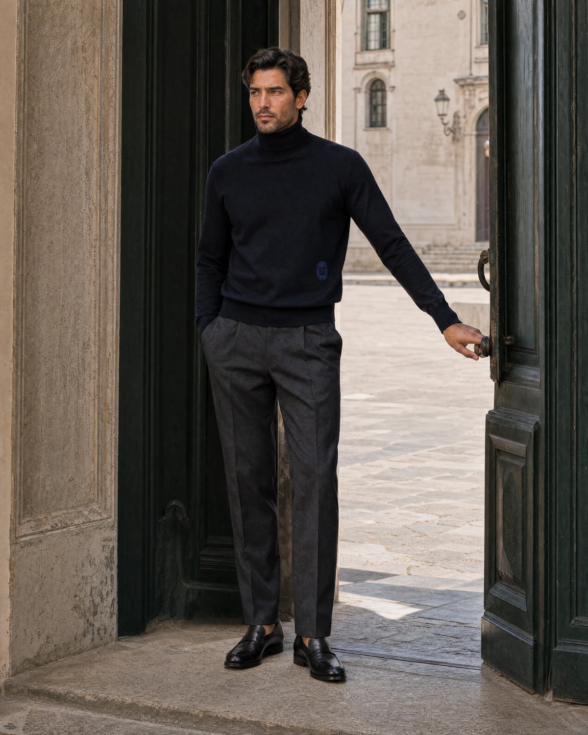 Man wearing a navy turtleneck and charcoal trousers beside a palazzo doorway