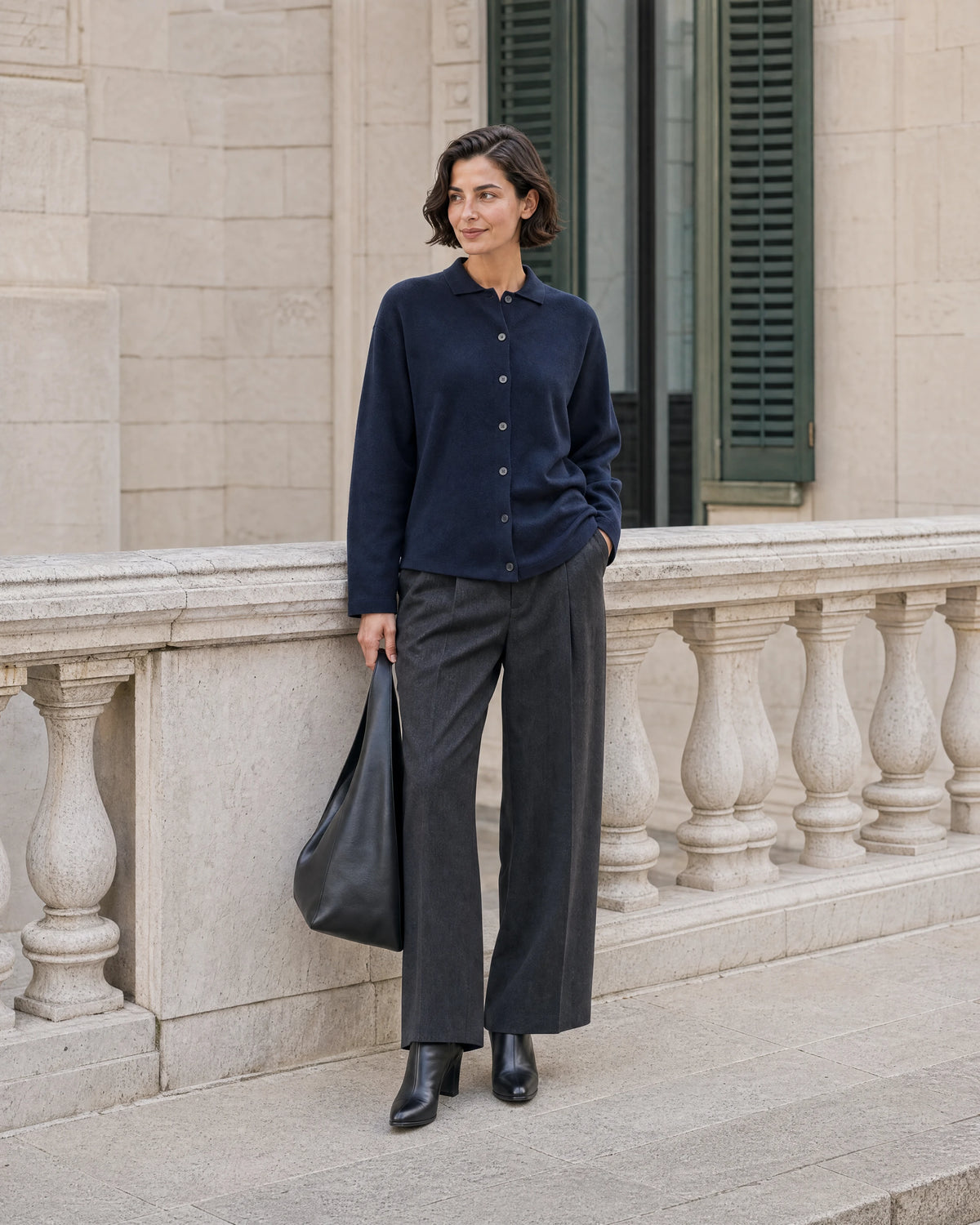 Woman wearing a navy cardigan and tailored trousers beside a stone balustrade