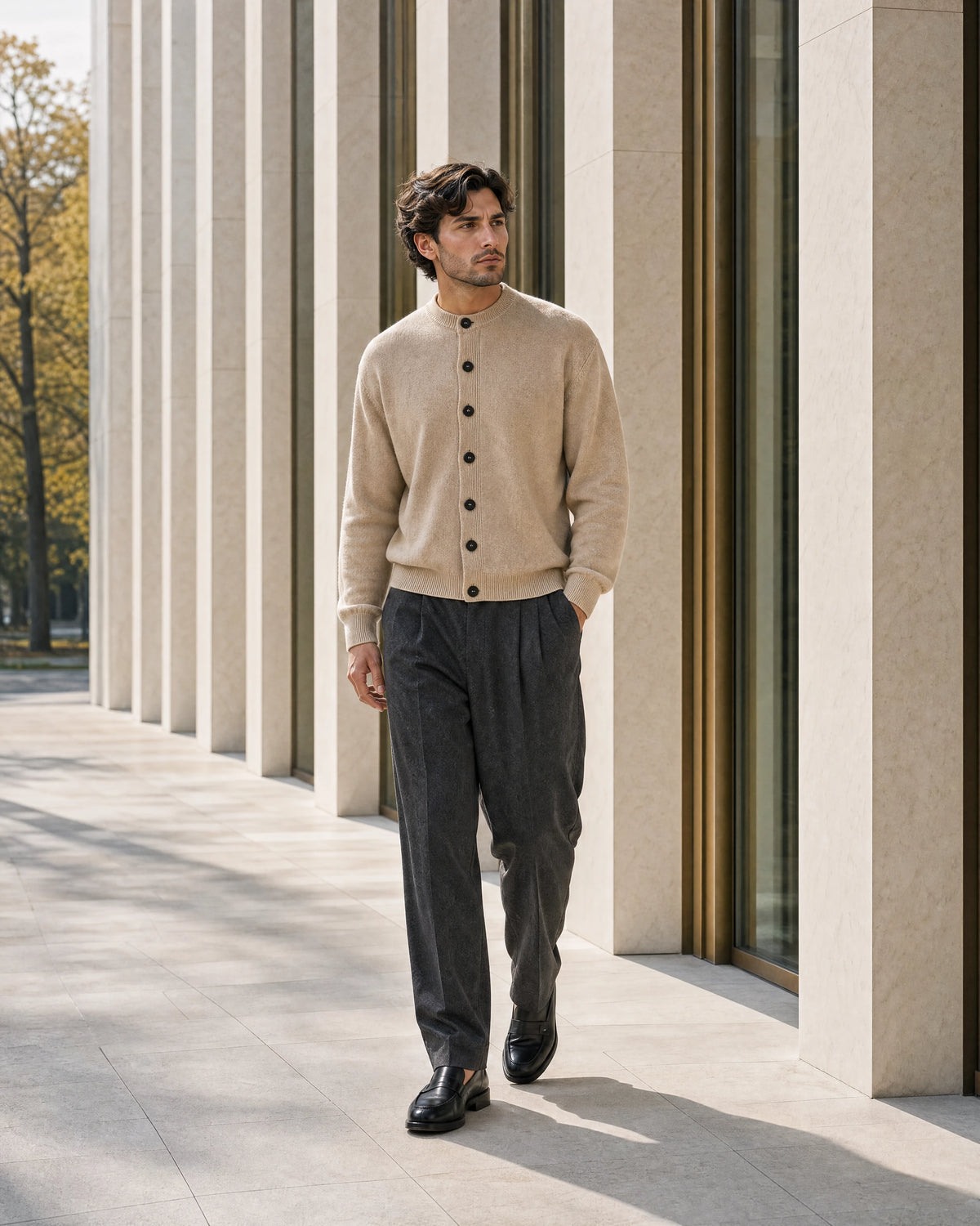 Man wearing a beige cardigan and charcoal trousers along a modern Italian colonnade